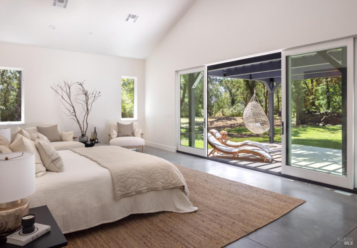 A bedroom with a large bed, cozy seating, and sliding glass doors leading to an outdoor patio.