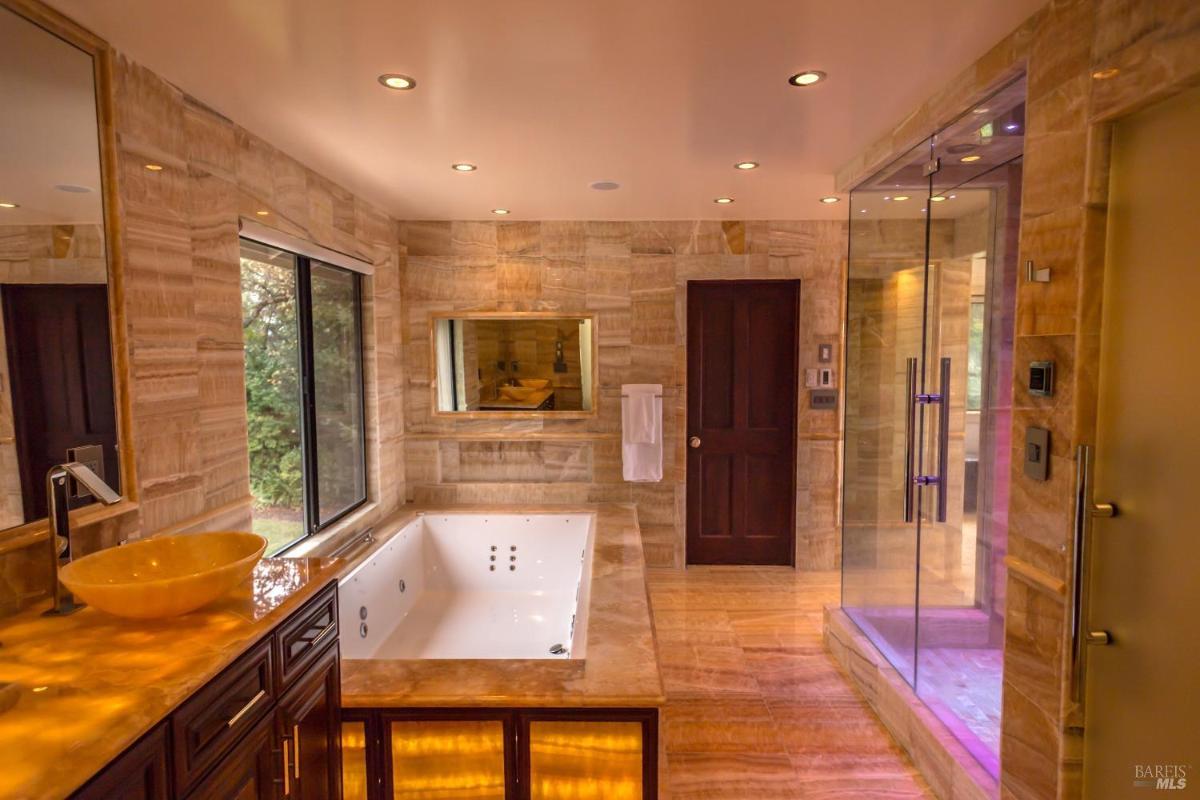 A bathroom featuring a large bathtub, a glass shower, a sink with a bowl design, and wooden cabinetry. 