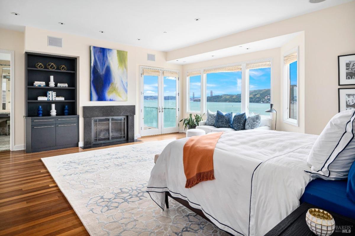 Bedroom with a bed, fireplace, and windows overlooking the ocean with a view of a bridge.