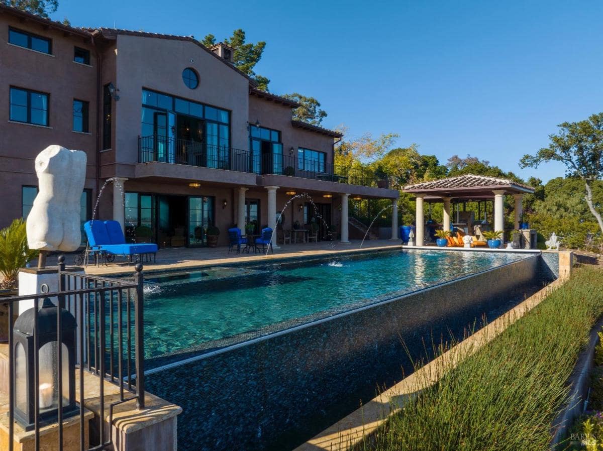 Large pool with fountain features next to a covered outdoor lounge area.