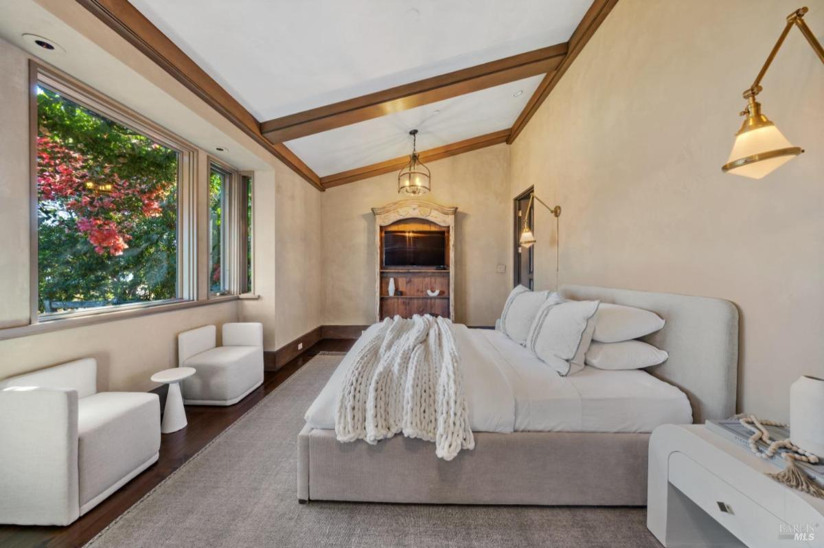 A modern bedroom with a plush bed, light-colored bedding, and two stylish chairs.