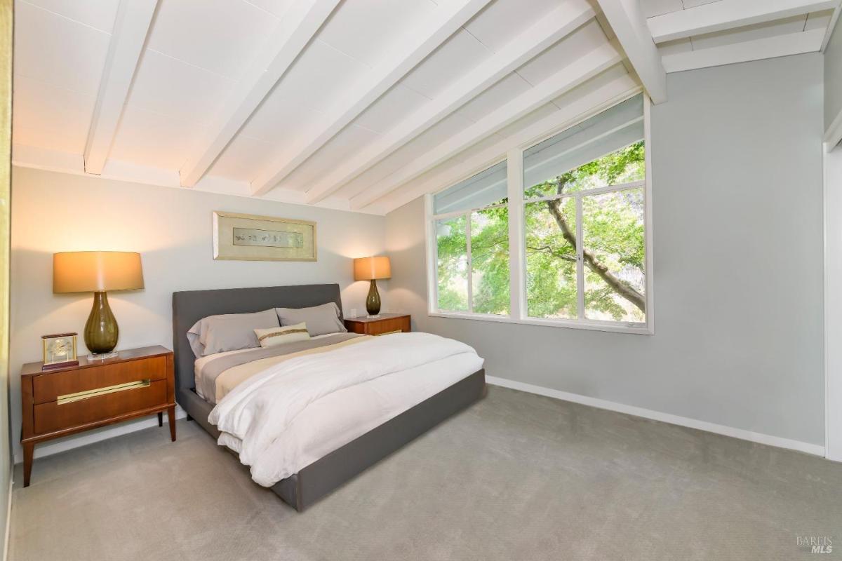 A bedroom with a large bed, windows overlooking greenery, and two side tables with lamps.