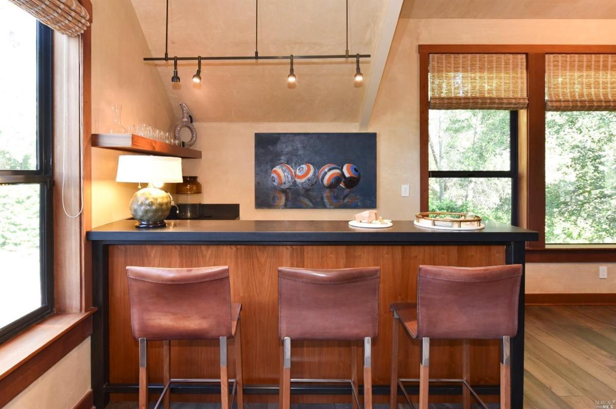 A home bar with three bar stools, a counter, and a painting on the wall.