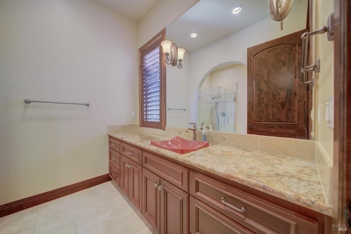 A bathroom with a spacious vanity featuring a countertop, a unique sink, and wooden cabinetry, along with a mirror and soft lighting.