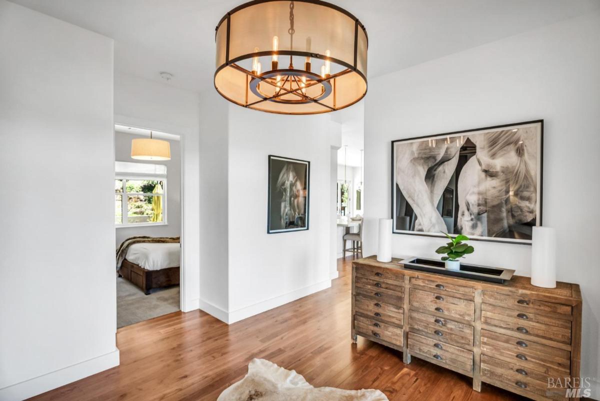 A hallway features a wooden dresser, artwork on the wall, and light fixtures above. 