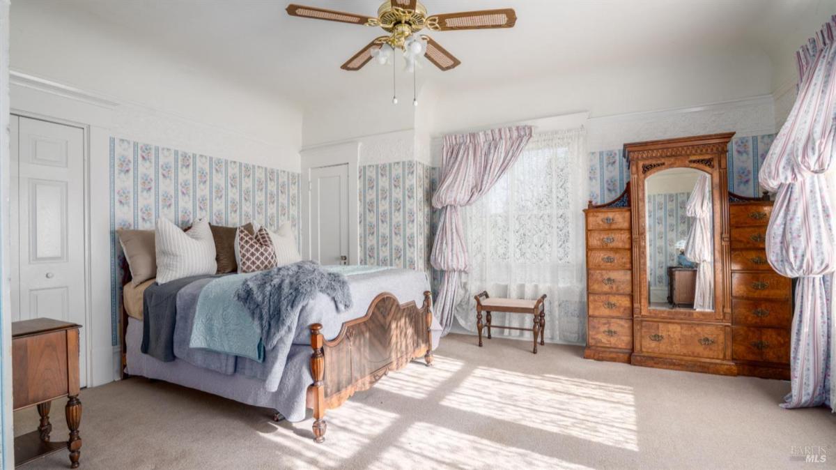 Bedroom with floral wallpaper, bed, and wooden dresser.