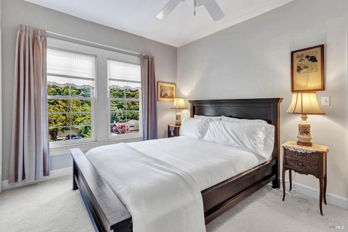 A bedroom with a dark wood bed frame, white bedding, and windows with curtains.