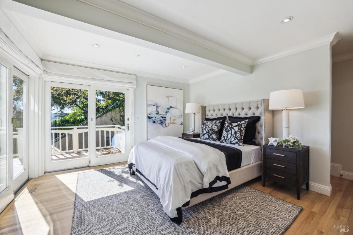 A second bedroom with a tufted headboard, side tables, and access to a balcony through glass doors.