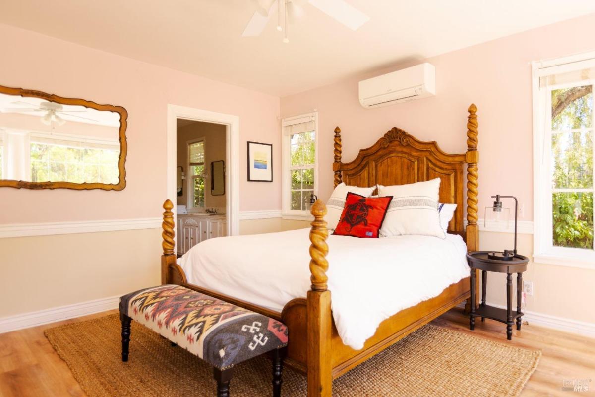 A bedroom with a wooden bed frame, a patterned bench, and a view of a connected bathroom.