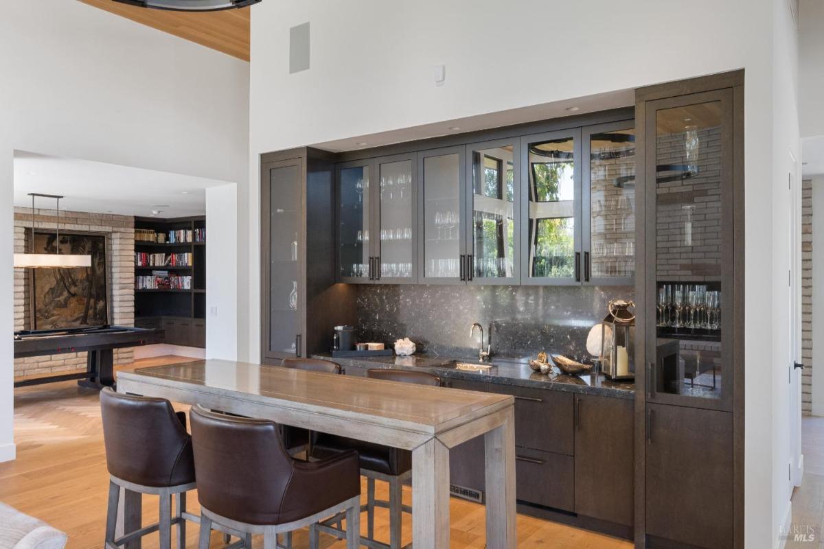 A built-in bar area with glass-front cabinets, a sink, and a wooden table with bar stools.