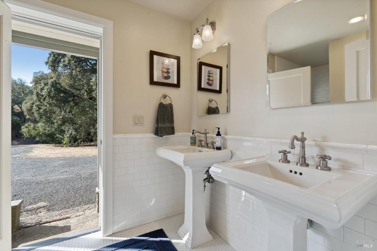 A bathroom with double pedestal sinks and a door to an outdoor area.