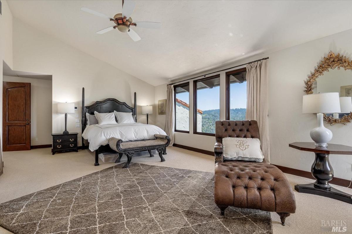 A bedroom with a bed, chaise lounge, and large windows with outdoor views.