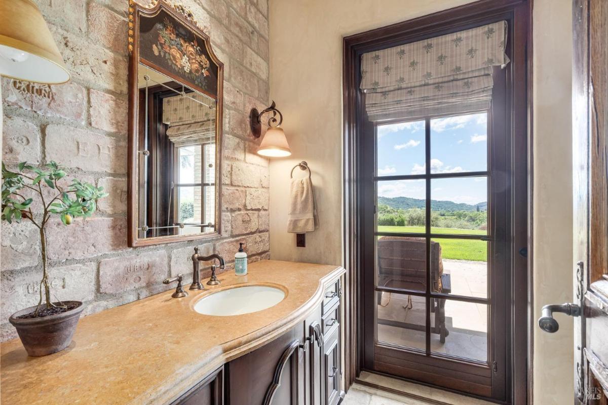 A bathroom with a sink, counter, mirror, and a glass door showing an outdoor view.