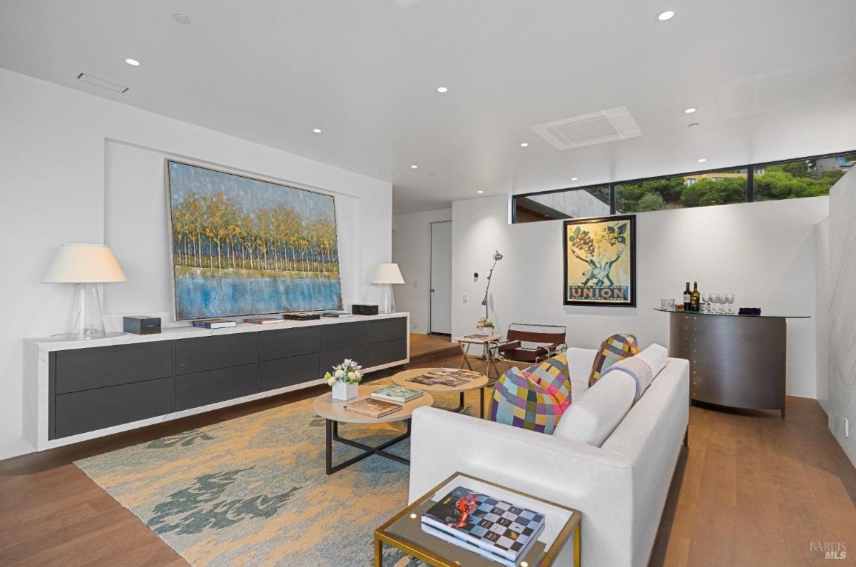 A family room with a wall-mounted credenza, a large framed painting, and a white sofa.