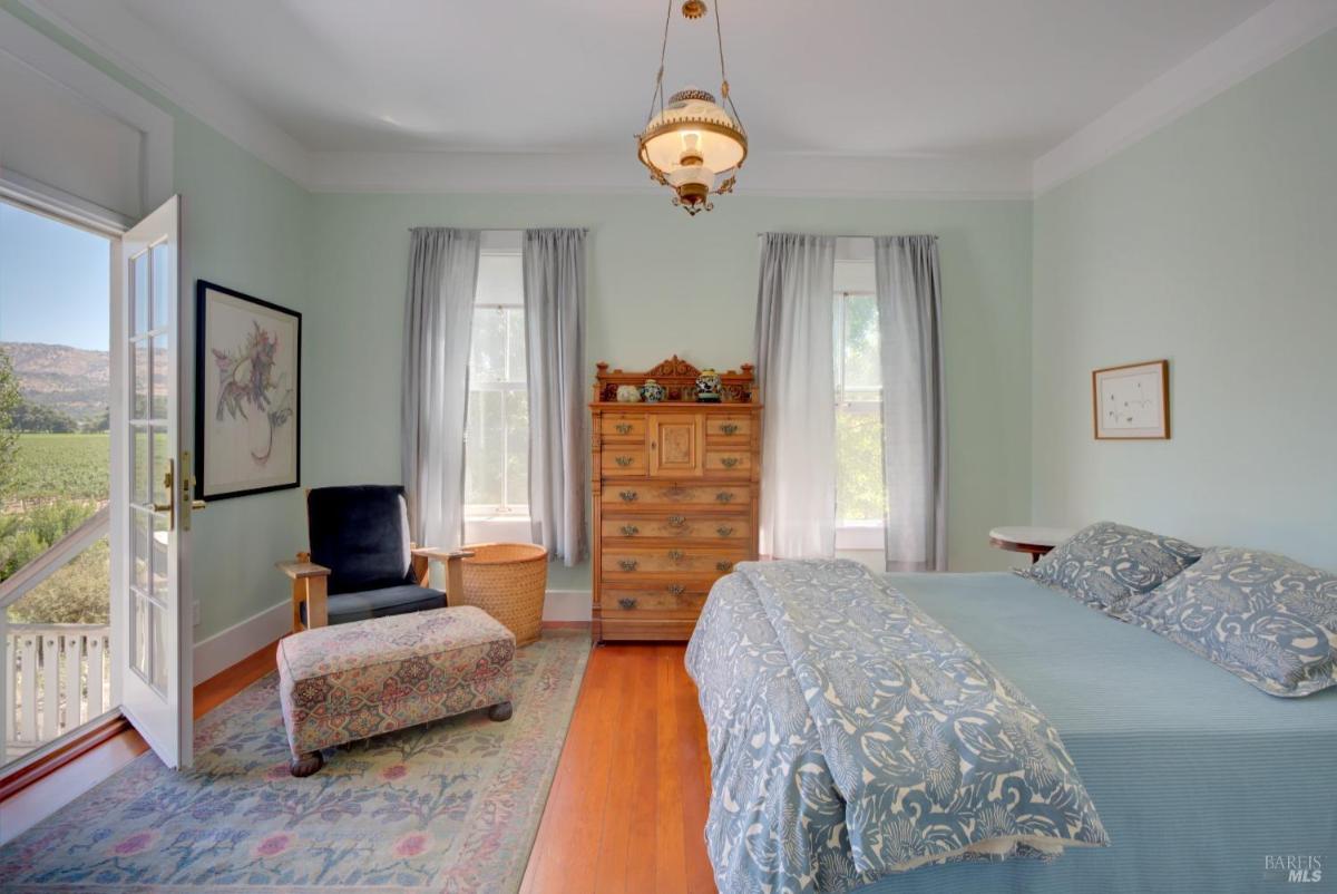 A bedroom with light green walls, a bed, a dresser, a chair, and a door leading to a balcony with a view.