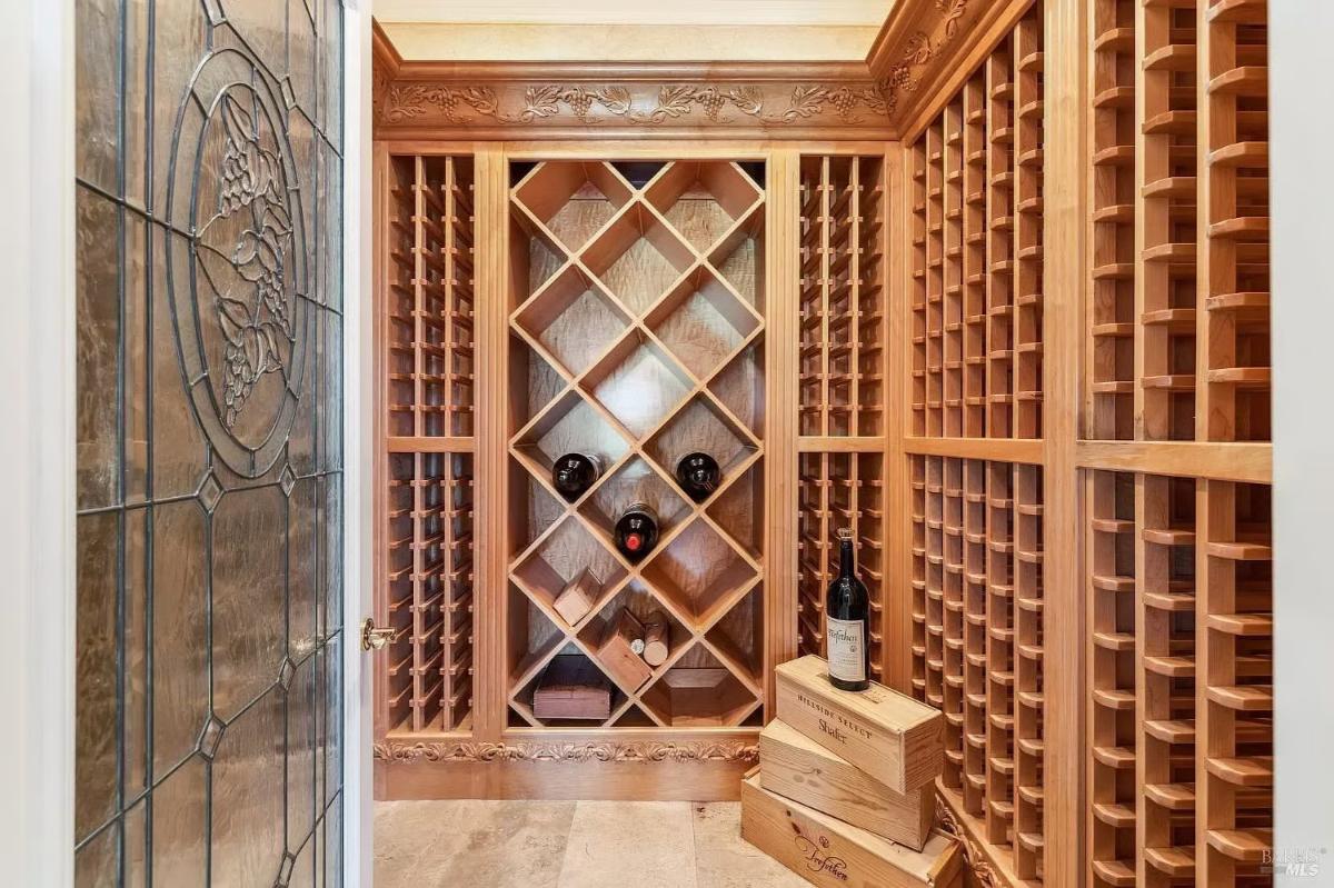 Wine storage room with wooden racks holding bottles and decorative glass-paneled door.