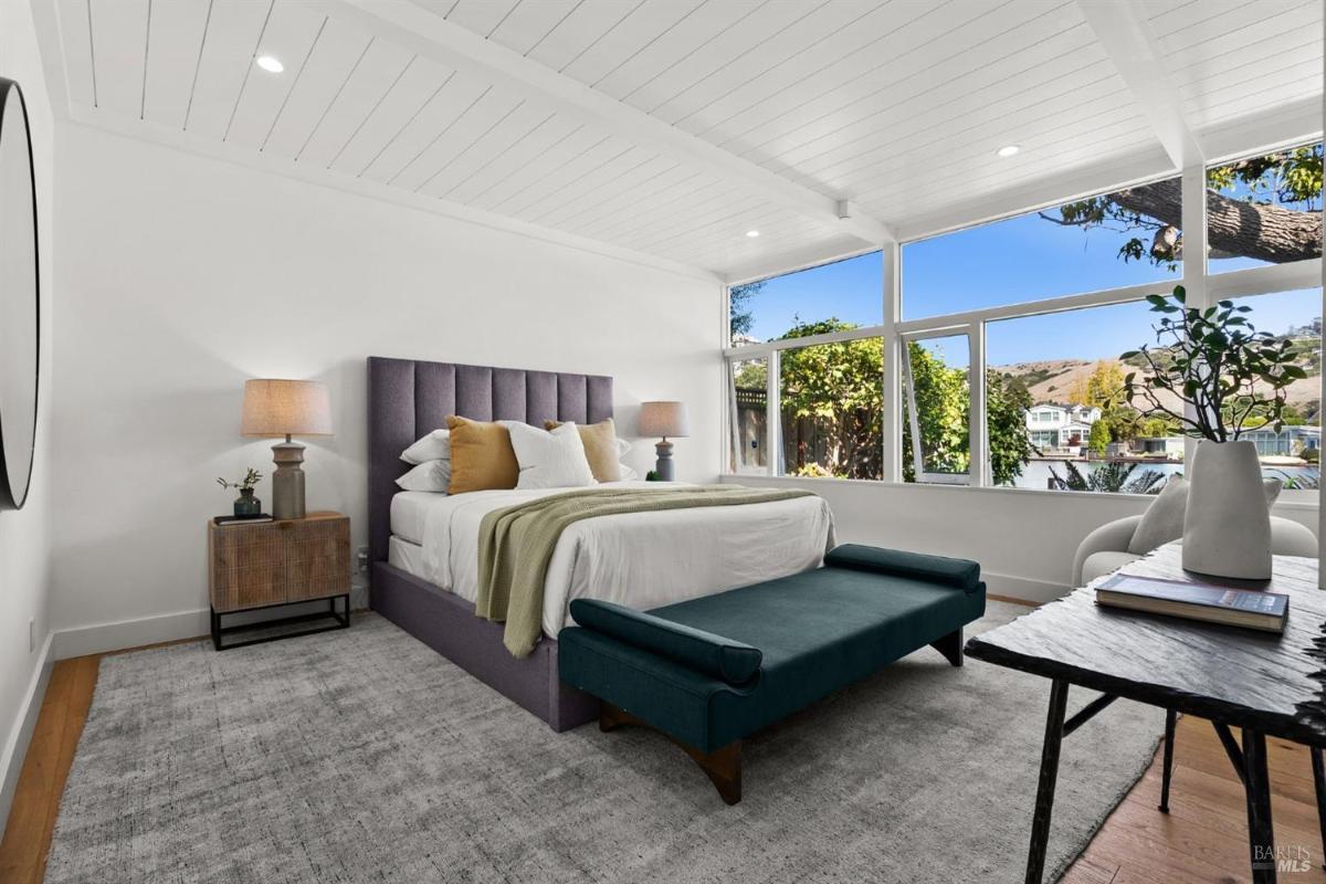 A bedroom featuring a purple upholstered bed, large windows, and a bench at the foot of the bed.