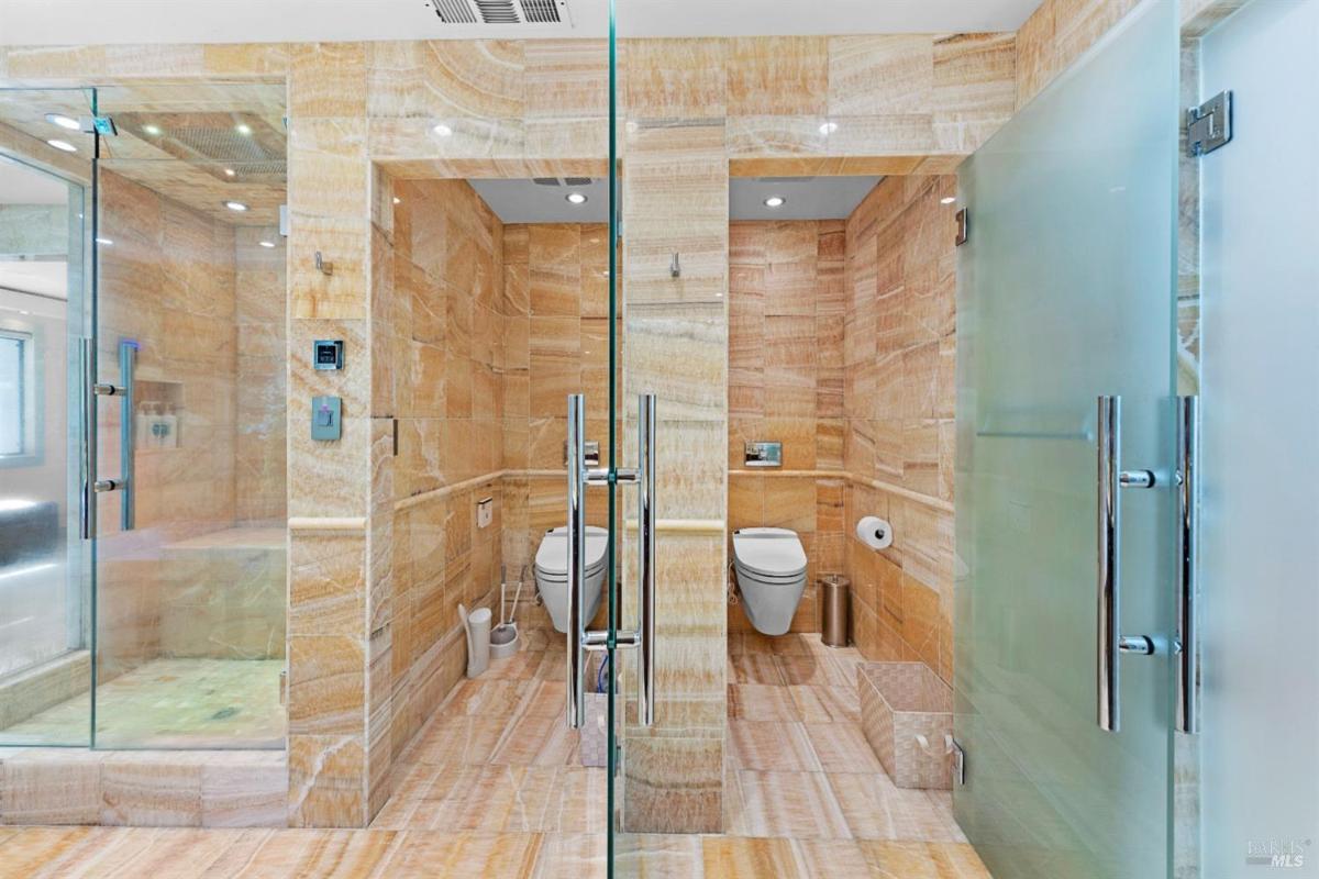 A bathroom with a glass shower, two toilets, and a sink area, all featuring stone walls. 