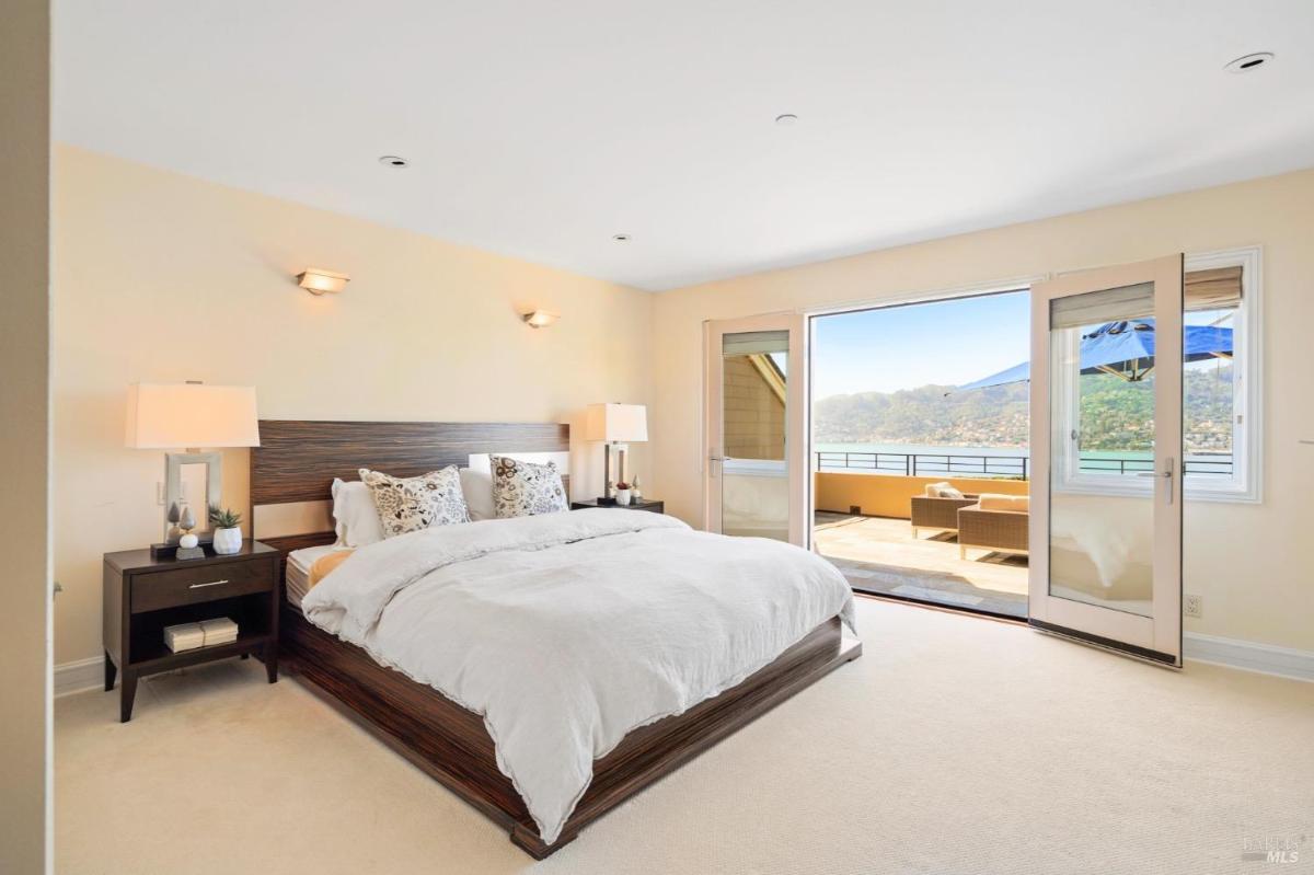 Bedroom with a wooden bed, nightstands, and an open door leading to a terrace with ocean views.