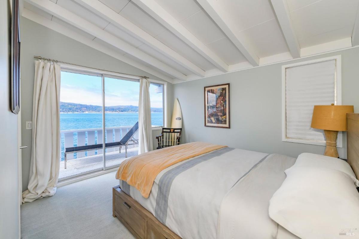 A bedroom with a bed, art on the wall, and sliding doors opening to a deck with a water view.