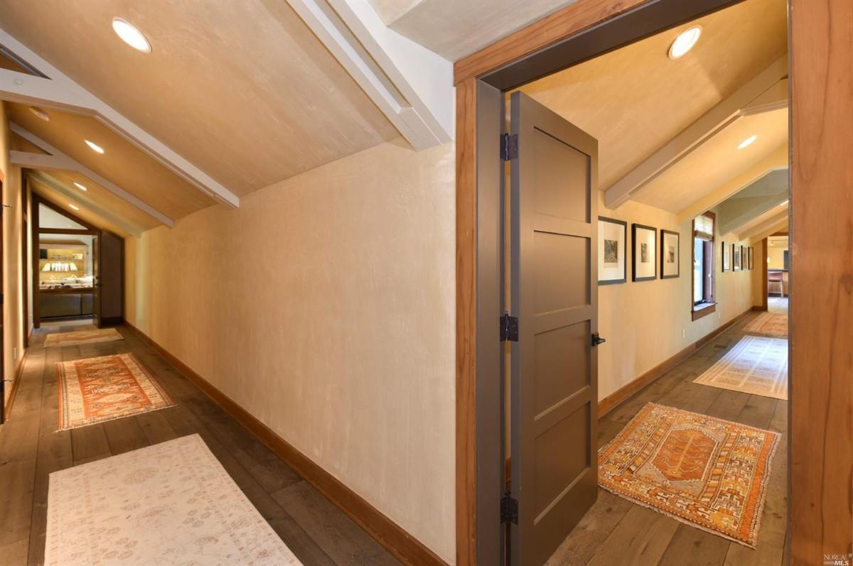 A long hallway with sloped ceilings, rugs, and doors on either side.