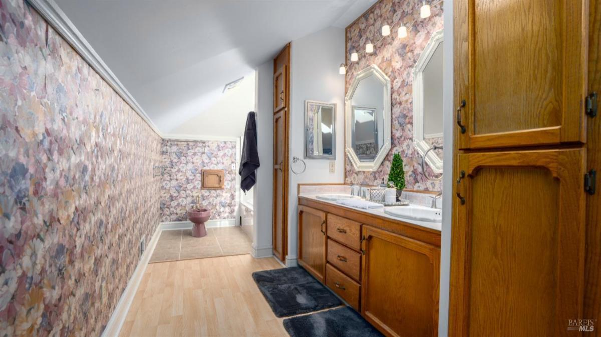 Bathroom with floral wallpaper, dual sinks, and storage cabinets.