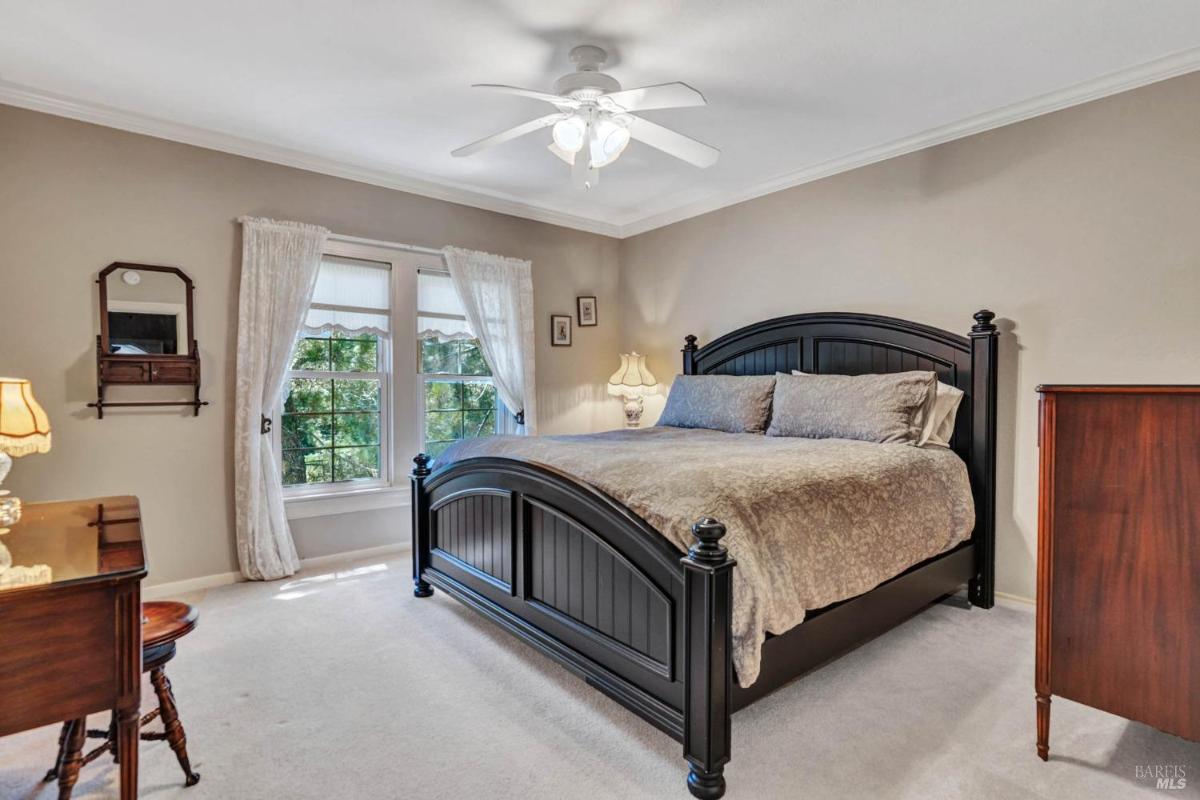 A bedroom featuring a dark bed frame, neutral bedding, and natural light from windows.