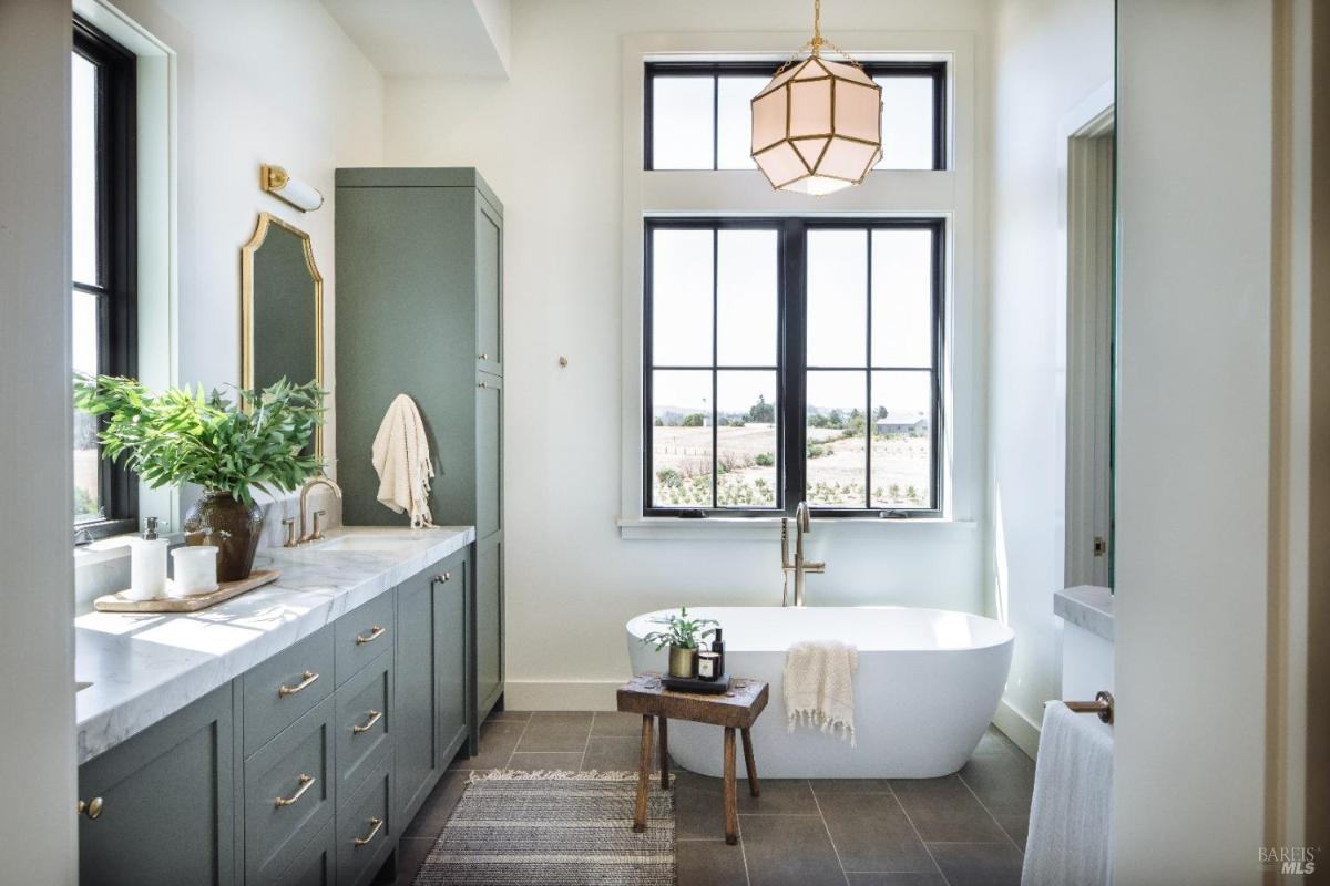 A modern bathroom featuring a freestanding tub, large windows, and green cabinetry.