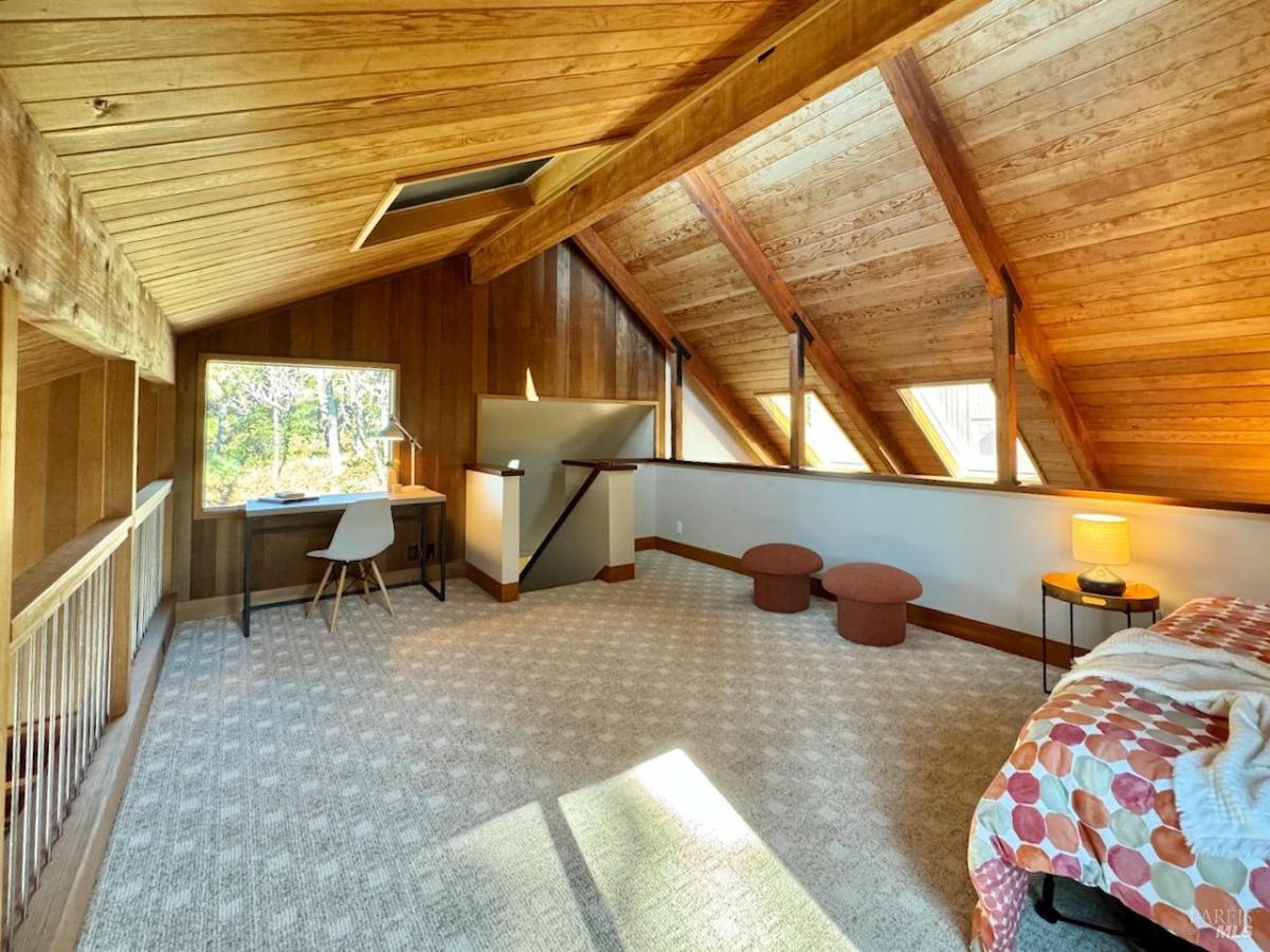 A bedroom with a sloped wooden ceiling, a window, and a bed with orange accents.