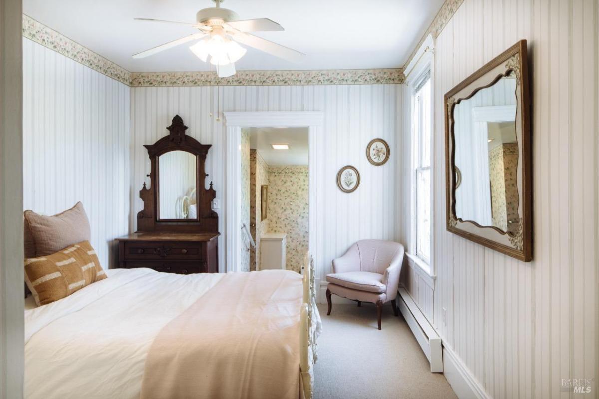 A bedroom with floral wallpaper, a vintage dresser, and an upholstered chair.