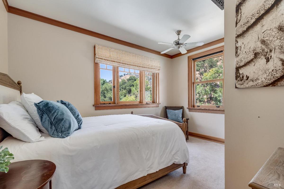 Bedroom with a bed, ceiling fan, and windows showing outdoor views.