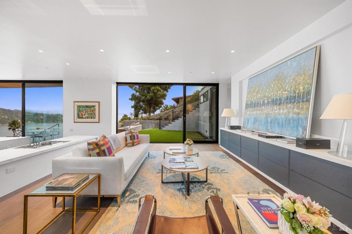 A family room with a white sofa, patterned pillows, and sliding glass doors leading to outside yard.