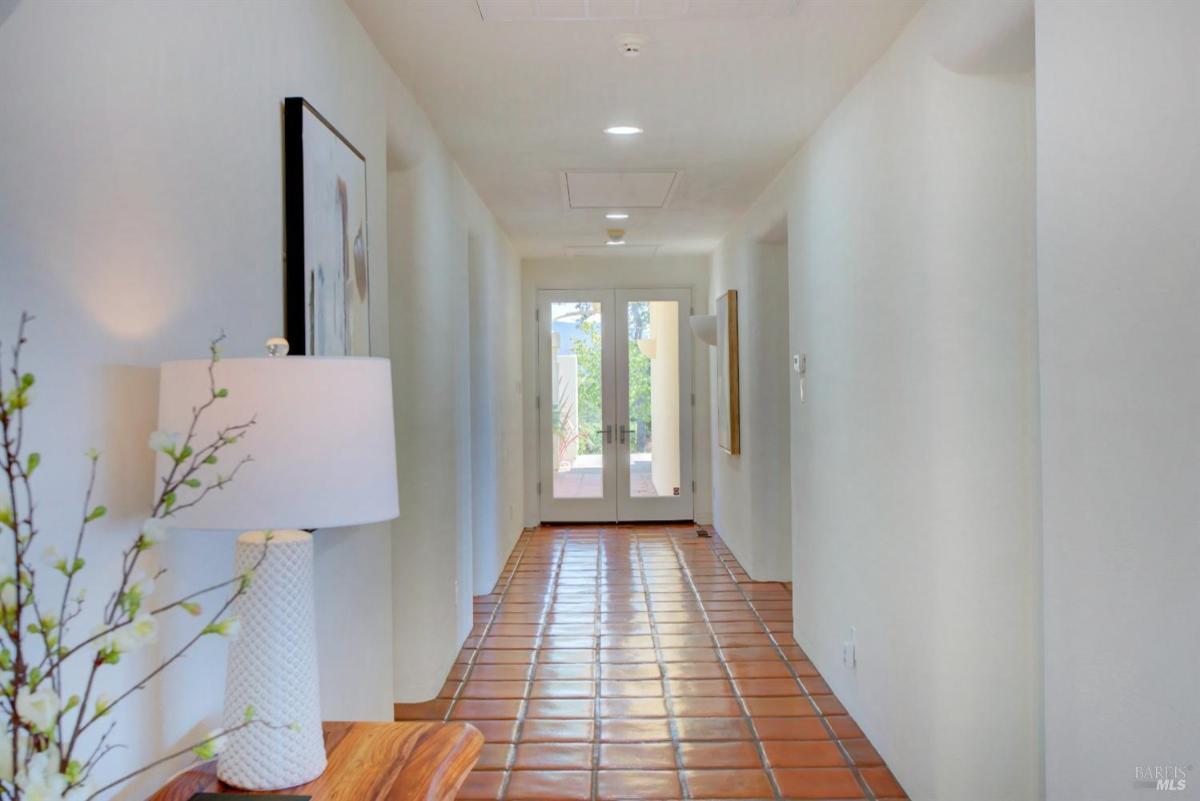 A hallway with terracotta tile flooring and double doors at the far end.