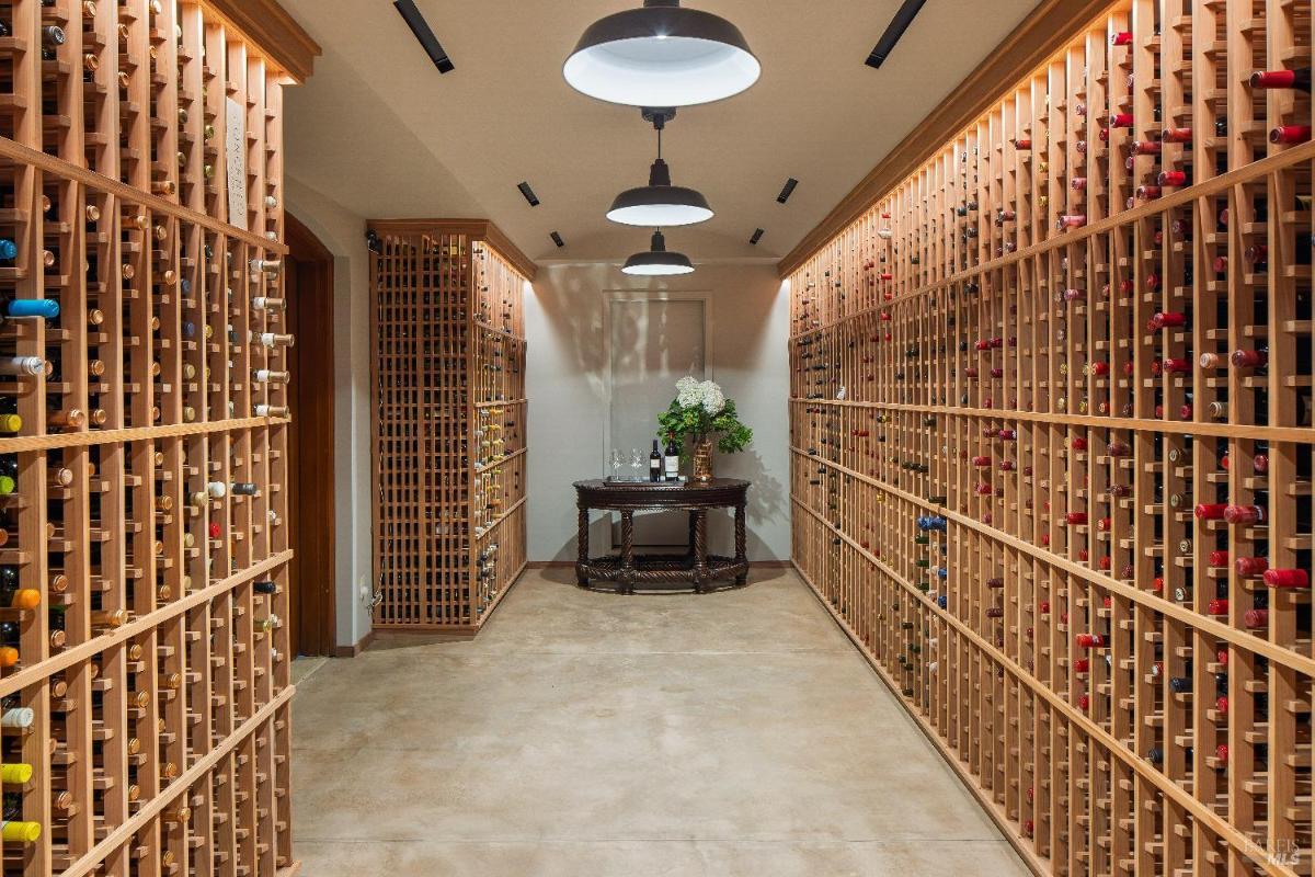 Wine cellar with wooden racks lining both walls and a small table in the center.