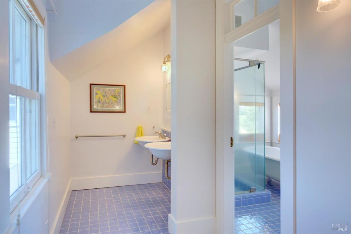 A bathroom with blue tiled floors, a sink, a glass-enclosed shower, and a freestanding bathtub.