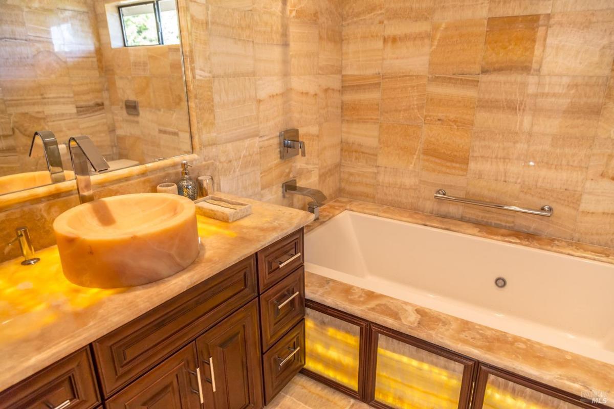 A bathroom featuring a large stone sink bowl, a wooden vanity with drawers, and a bathtub. 