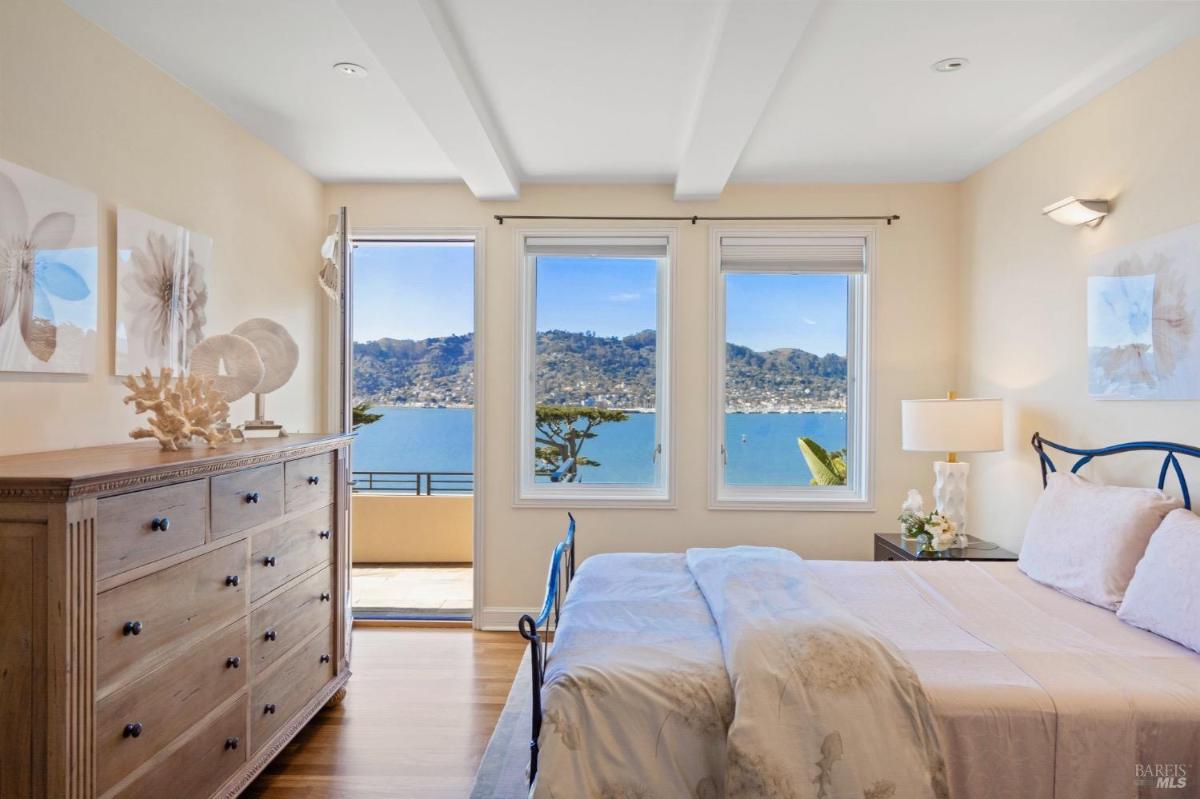 Bedroom with a dresser, bed, and two windows facing a mountain and ocean view.