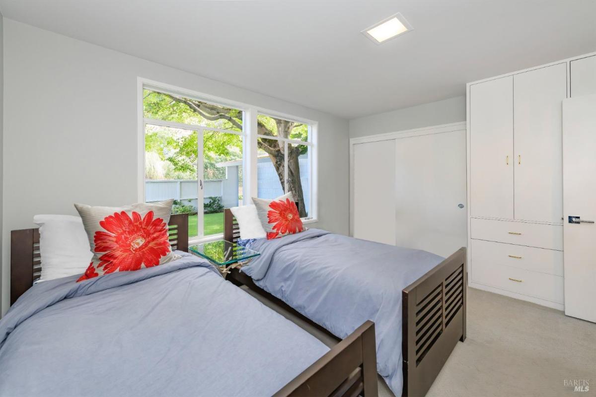 A bedroom with two twin beds, a large window with a garden view, and built-in closets.