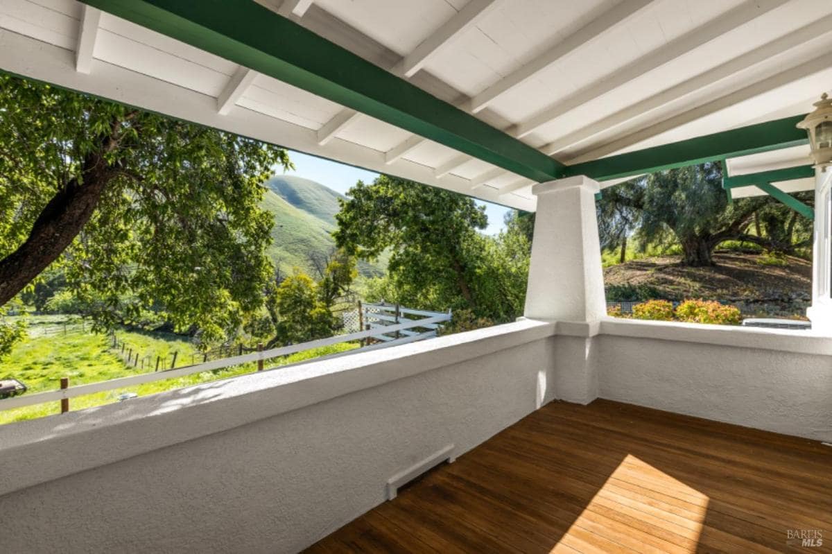 Covered patio with wooden flooring and views of trees and hills.