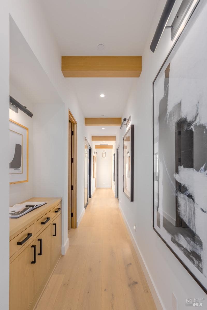 A hallway with wood beams, recessed lighting, framed artwork, and built-in cabinetry.