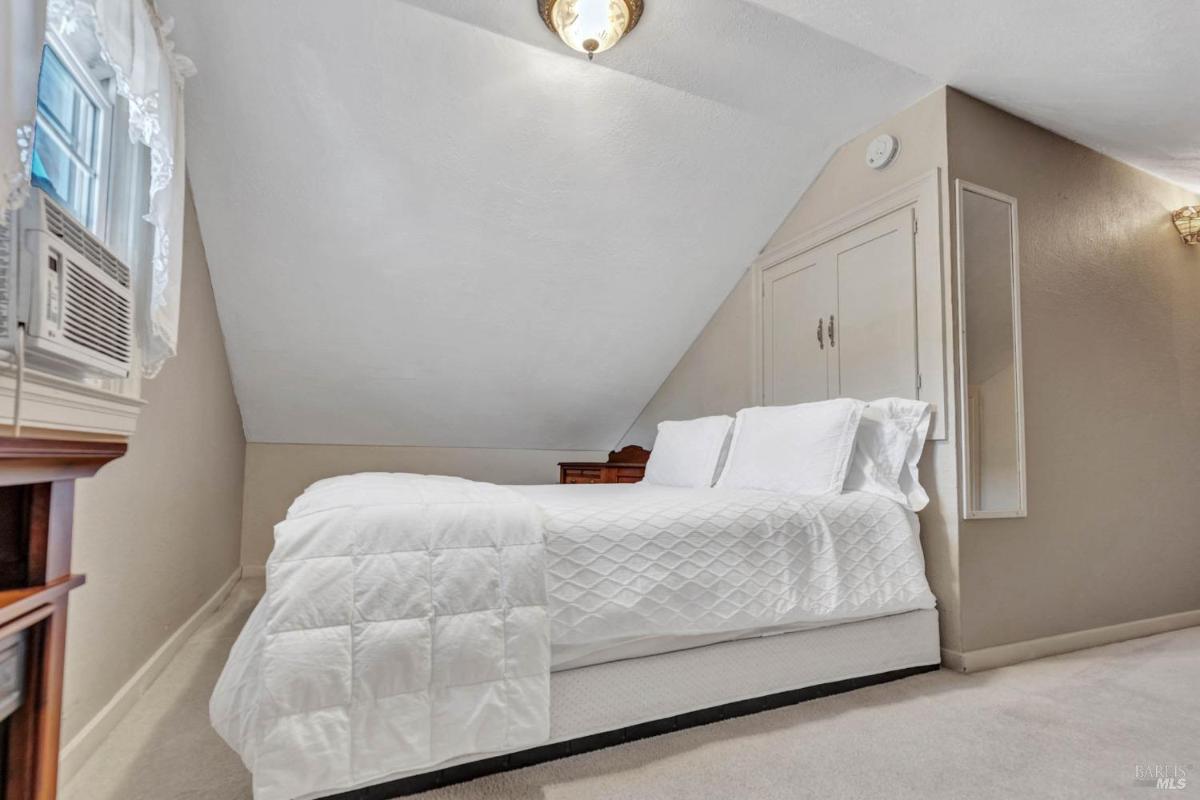 An attic bedroom with a sloped ceiling, white bedding, and a small closet.