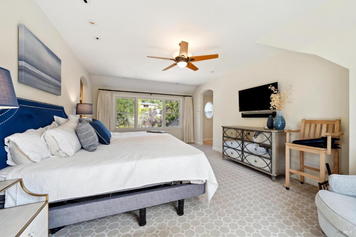 A bedroom with a neutral color palette, arched window, and seating area near the bed.