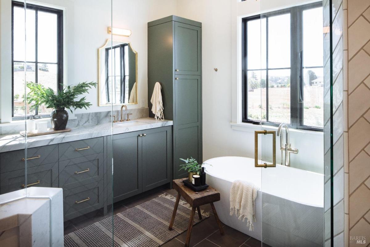 A modern bathroom featuring a freestanding tub, large windows, and green cabinetry.