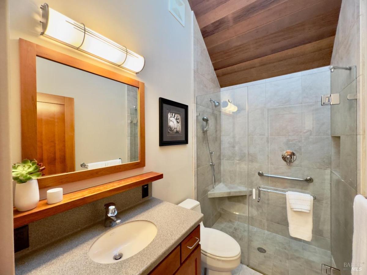 A bathroom with a glass shower enclosure, sink, and wooden ceiling.