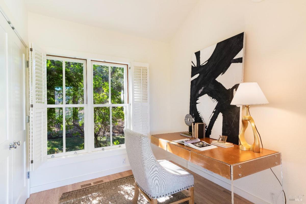 Workspace with small desk with a chair near windows with shutters and a large abstract painting.