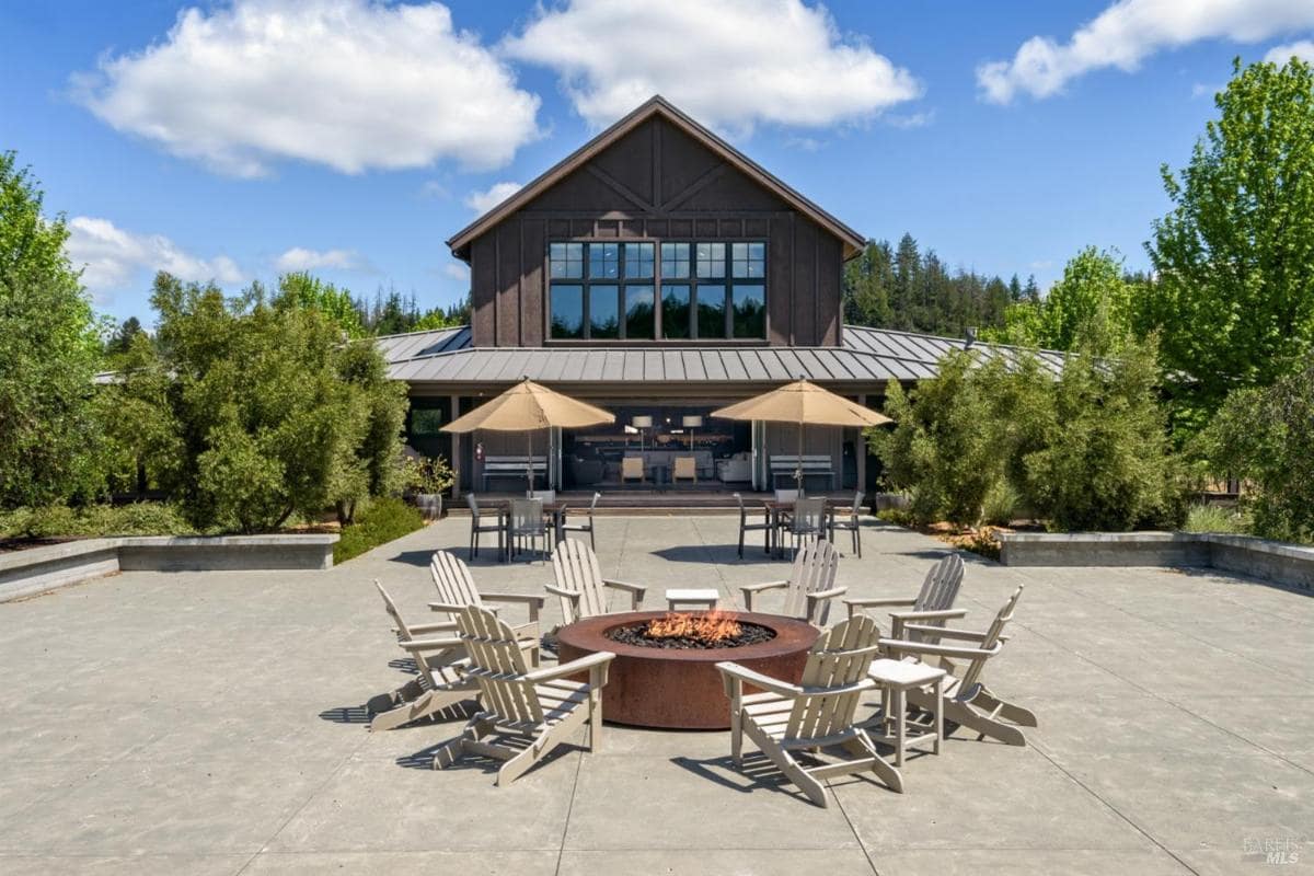 Fire pit area surrounded by chairs on a patio with a building in the background.