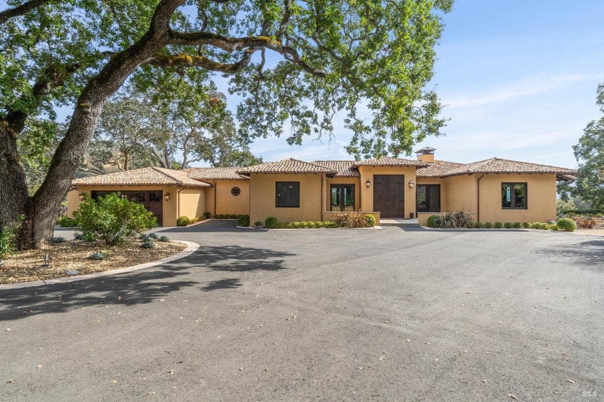 A single-story stucco house with a circular driveway and mature trees.