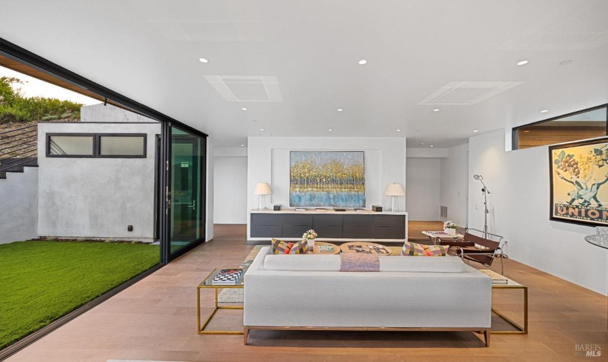 A family room with a white sofa, a wall-mounted credenza, a large painting, and sliding doors opening to outside yard.