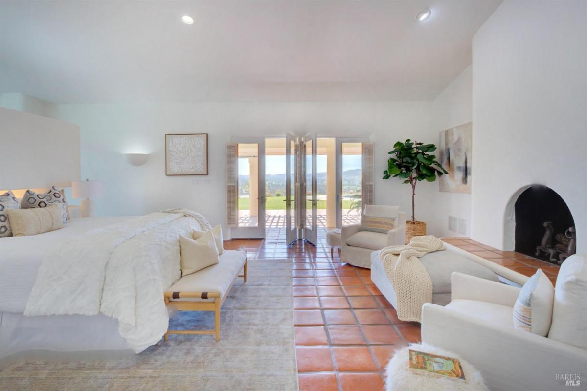 A bedroom with a fireplace, seating, and doors opening to an outdoor patio.