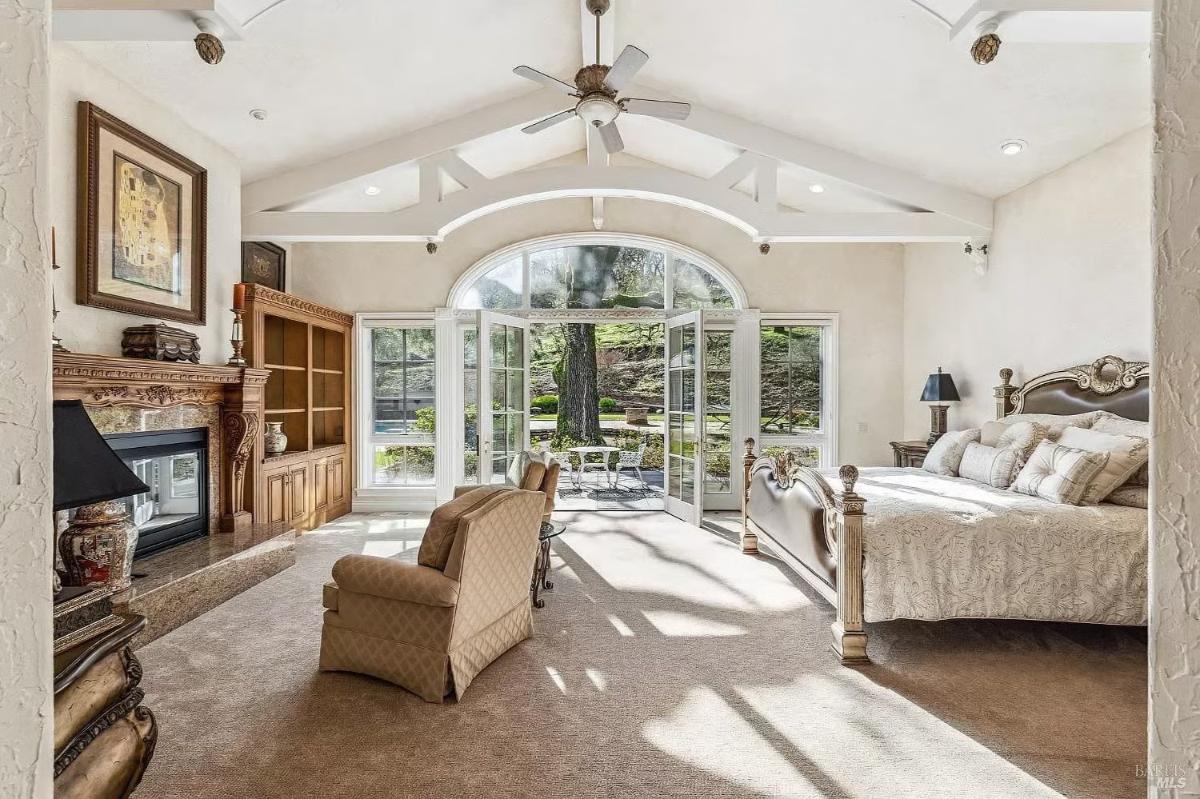 Bedroom with a king-sized bed, high ceilings, a fireplace, and French doors leading to an outdoor seating area.